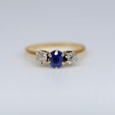 three stone ring on white surface with one blue sapphire and the other two white diamonds