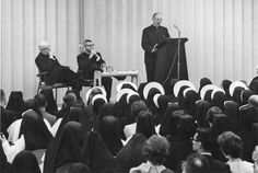 two men standing at podiums in front of a group of people wearing black robes