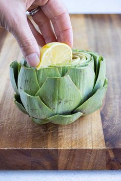 a person cutting up an artichoke with a lemon wedge on top of it