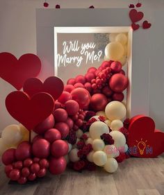 valentine's day balloon arch with hearts and flowers in front of a sign that says will you marry me?