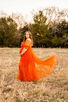 a woman in an orange dress is standing in a field with her arms around her waist