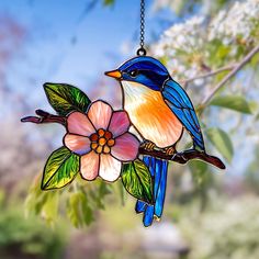 a stained glass bird sitting on a branch with flowers hanging from it's side