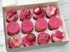 a box filled with pink cupcakes on top of a wooden table next to a white wall