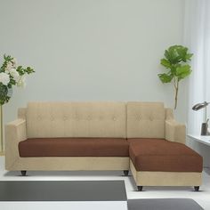 a brown and tan couch sitting in front of a white wall next to a potted plant