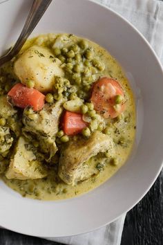 a white plate topped with chicken and peas covered in gravy next to a fork