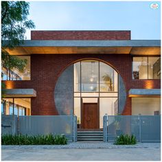 the entrance to a modern home with large circular window and brick facade, surrounded by greenery