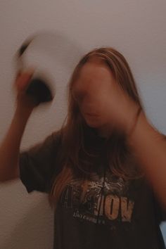 a woman holding a white frisbee in her right hand while standing next to a wall