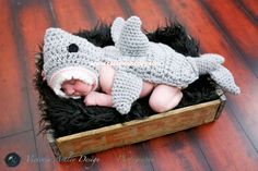 a baby in a crocheted shark hat laying on top of a wooden crate