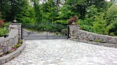 a stone driveway with an iron gate and brick walkway leading to the entrance into a wooded area