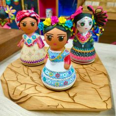 three figurines sitting on top of a wooden tray with flowers in their hair