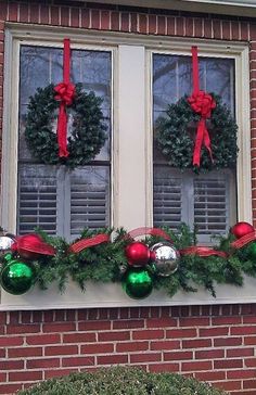 two christmas wreaths are hanging on the window sill in front of a brick building