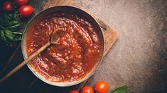 tomato sauce in a pan with basil and tomatoes around it on a wooden cutting board