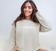 Elevate your bridal style with our 'In My Bride Era' sweatshirt - a chic blend of modern elegance and timeless tradition. Customize with your wedding date or last name on the sleeve accompanied by a sweet heart detail.  Makes a great gift for those newly engaged or a thoughtful addition to any wedding shower! The ideal gift for brides-to-be, this sweatshirt is a delightful way to share in the joy of their journey. Elevate your bridal style with this must-have! Taking care of your sweatshirt to ensure it stays cozy and stylish for the long run is easy. For best results, machine wash it inside out with like colors in cold water. Use a mild detergent and avoid bleach. Tumble dry on low heat, or hang it to air dry for optimal longevity. If needed, iron it on low heat, but avoid ironing directl Mrs Sweatshirt Brides, Bride Hoodie Sweatshirts, Future Mrs Sweatshirt, Bride To Be Sweatshirt, Aunt Sweater, Bride Era, Aunt Sweatshirt, Grandma Sweater, Nursing School Gifts