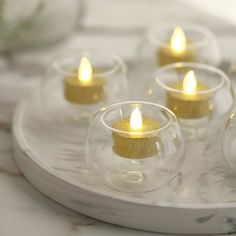 small glass tealight candles on a tray with gold glitter in the middle and one lit