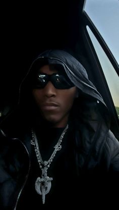 a man wearing sunglasses and a hoodie in the back seat of a car with a chain on his neck