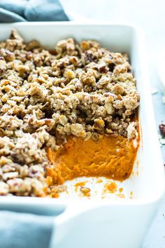 a casserole dish filled with sweet potatoes and crumbled nuts on top