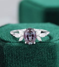 a ring with an oval shaped purple stone surrounded by white diamonds on a green velvet box