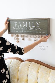 a woman holding up a family calendar on a wall mounted to the side of a couch