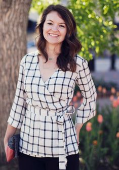 a woman standing in front of a tree wearing a white and black checkered top