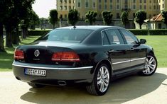 a black car parked in front of a large building with trees on the other side