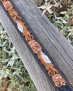 a brown and black leather belt with feathers on the side, sitting on top of a wooden