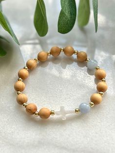 a wooden beaded bracelet with two beads and a cross on the front, sitting next to a plant