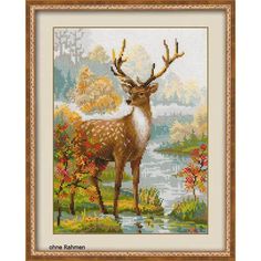 a deer with antlers standing in front of a body of water and autumn trees