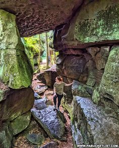 a person standing in the middle of a cave with large rocks and moss growing on it