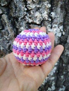 a hand is holding a small crochet ball in front of a tree trunk