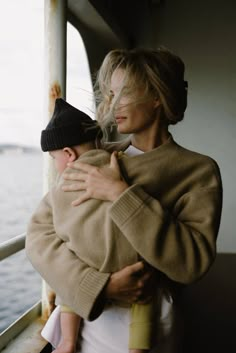 a woman holding a baby in her arms while standing on a boat near the water