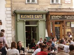 a group of people sitting at tables in front of a restaurant on a city street