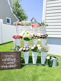 a bunch of flowers that are sitting in buckets on the grass next to a sign