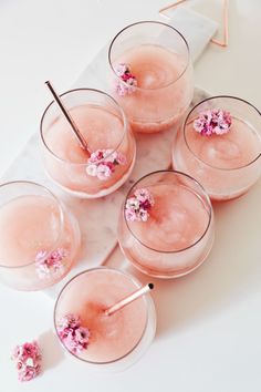 four glasses filled with pink drinks on top of a white table next to small flowers