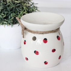 a white vase with red and black ladybugs on it next to a potted plant