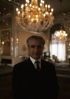 a man wearing a suit and tie standing in front of a chandelier