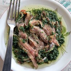 a white plate topped with meat and greens next to a fork on top of a table