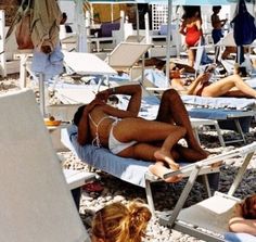 many people are lounging on the beach in chairs and umbrellas, while one woman is wearing a bathing suit