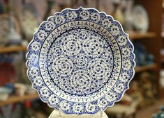 a blue and white plate sitting on top of a wooden stand in front of shelves