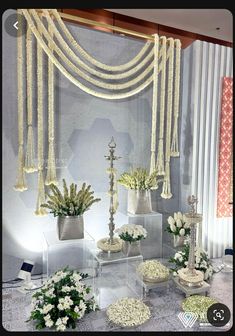 an arrangement of flowers and candles on display in front of a wall with white curtains