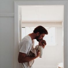 a man holding a baby in his arms while standing next to a doorway with the door open