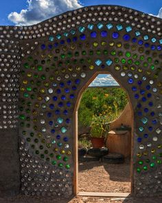 an arch made out of bottle caps in the middle of a desert area with blue sky and clouds