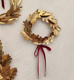 two wreaths made out of gold leaves and red ribbon tied around them on a white surface