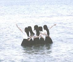 four girls are standing on a rock in the middle of the water, with their arms outstretched