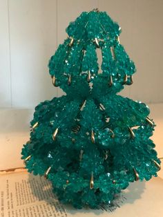 a green christmas tree made out of glass beads on top of an old book page