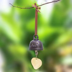 a bell hanging from a tree branch with a heart shaped charm attached to the bell