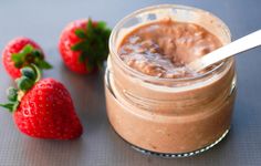 a jar filled with chocolate pudding next to two strawberries on a gray tablecloth