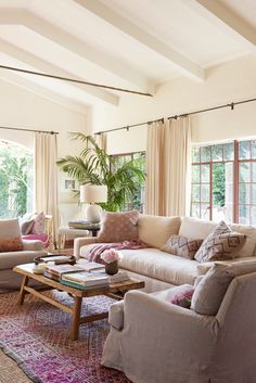 a living room with couches, chairs and rugs in front of large windows