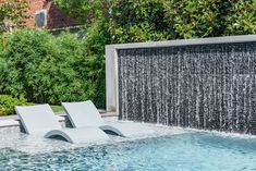 two lounge chairs sitting in the middle of a swimming pool with waterfall coming from it