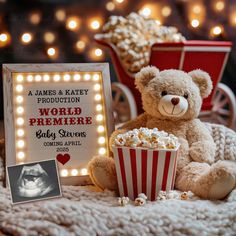 a teddy bear sitting on top of a blanket next to a box of popcorn and a sign