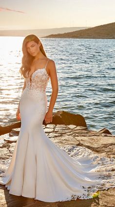 a woman in a wedding dress standing on rocks near the water